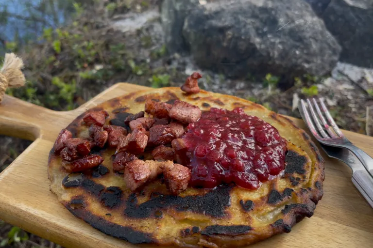 Kolbulle med bacon og lingonberry syltetøy på et trebrett på et steinete sted.