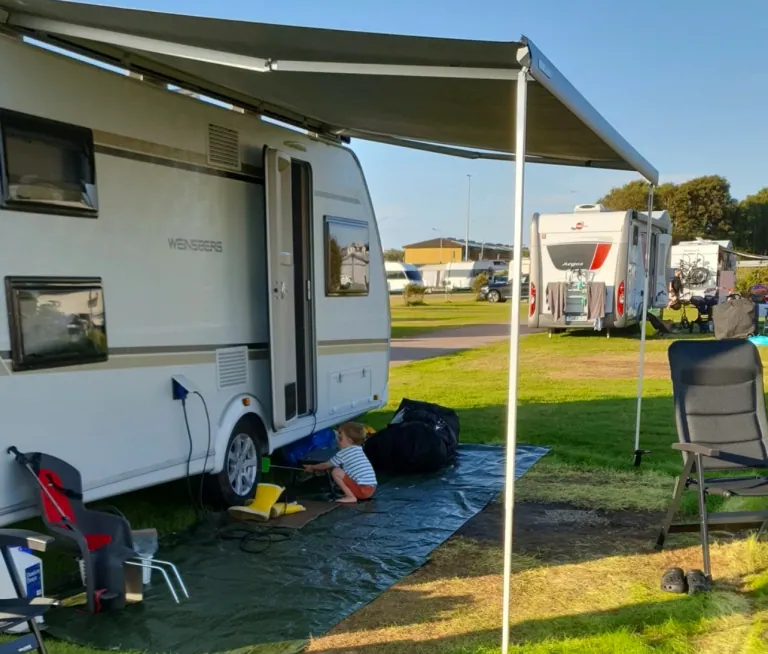 A caravan at a campsite with someone working underneath it and other caravans in the background.