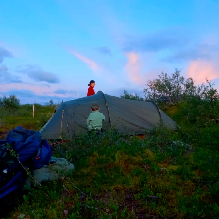 Twee mensen zetten een tent op in een schilderachtige omgeving onder een blauwe lucht.