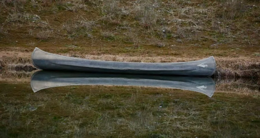 Ein Kanu ruht immer noch auf dem Wasser, reflektiert auf der Oberfläche, umgeben von üppigem Land.
