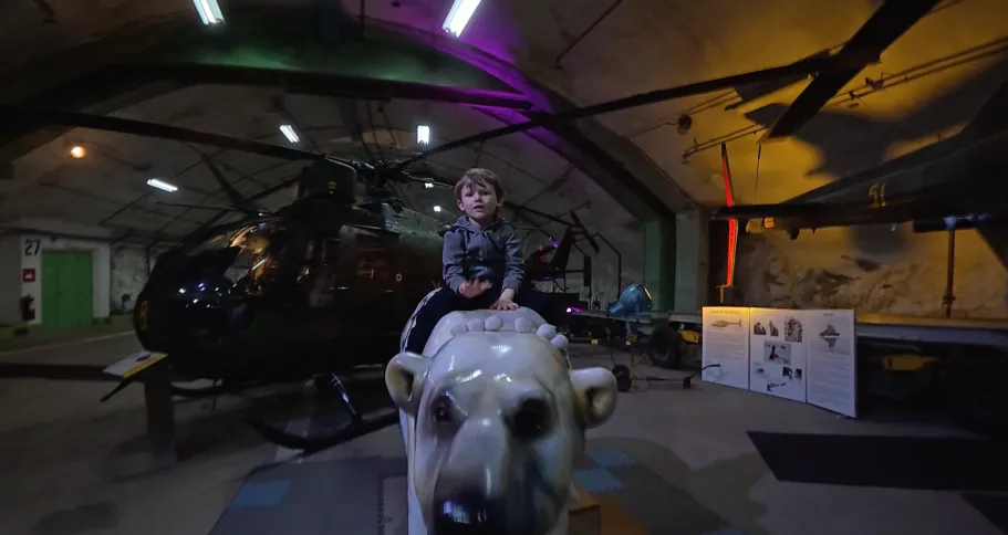 Barn sitter på en stor lejonstaty i ett museum med en helikopter i bakgrunden.