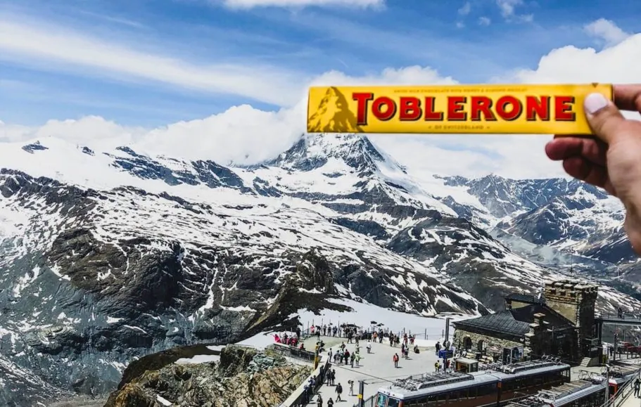 Ranka laiko Toblerone priešais Matterhorno sniegu padengtas viršūnes ir turistus.
