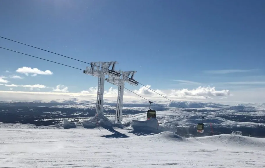 Skidbacke med gondollift och snöklädda fjärran berg under klar himmel.