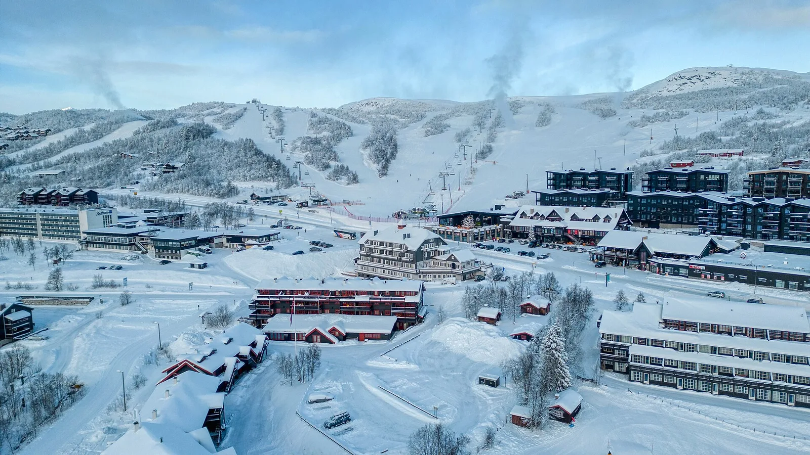 Beitostølen i vinterskrud med hotell och stugor i byn och skidbackarna på fjällsidan bakom.