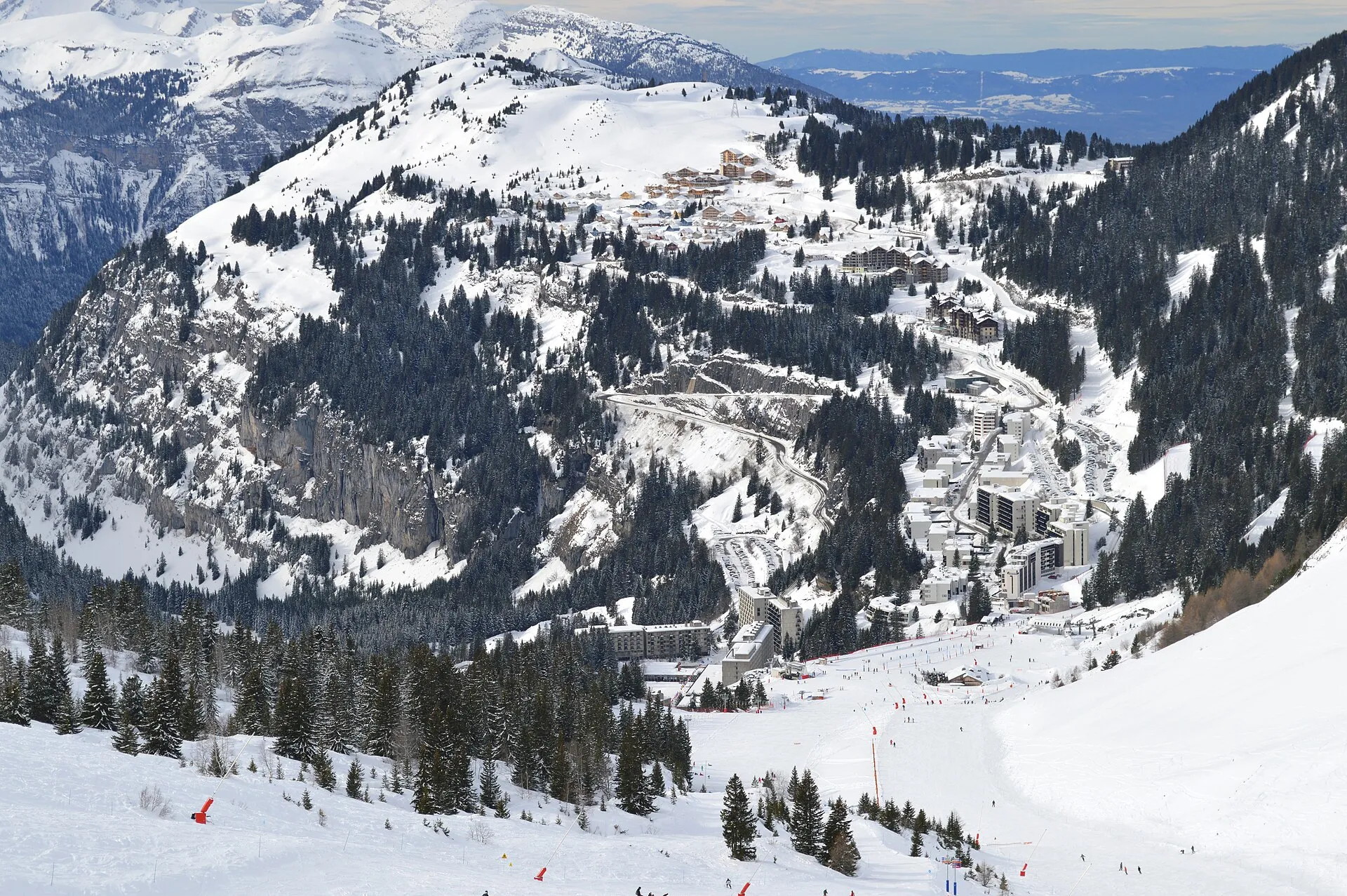 Skidbyn Flaine i en snötäckt skål omgiven av berg och granskog, med breda pister ner mot husen.