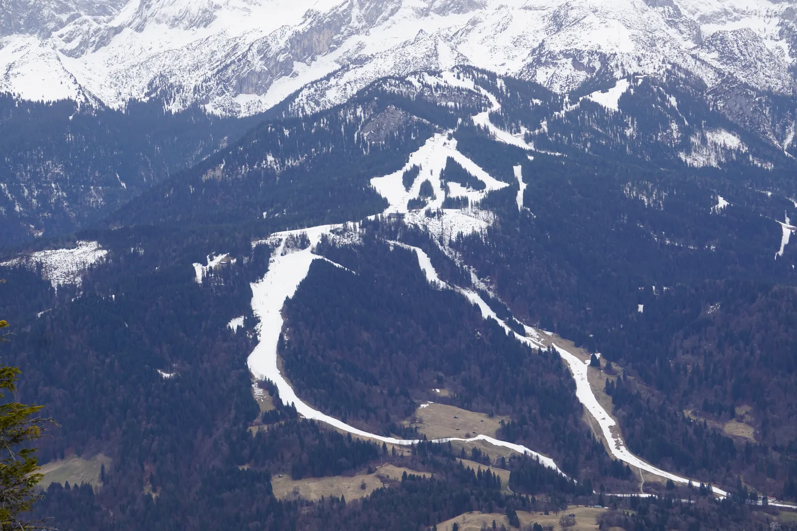 The ski slopes on the Hausberg in Garmisch-Classic seen from above, with white pistes winding down through the spruce forest and snowy mountains in the background.