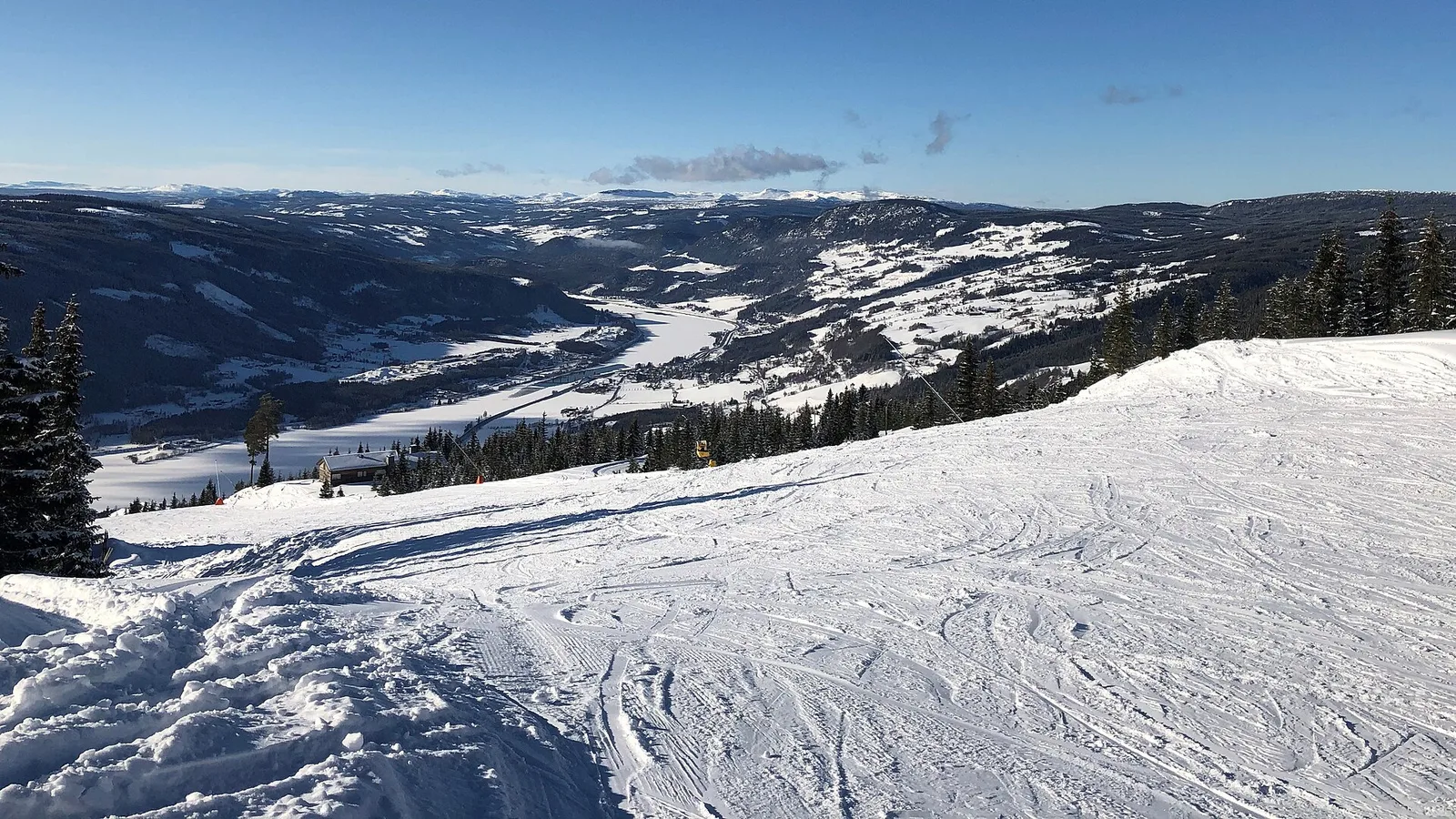 En nyåkt pist högt upp i Hafjell med utsikt över den snöiga dalen nedanför under blå himmel.