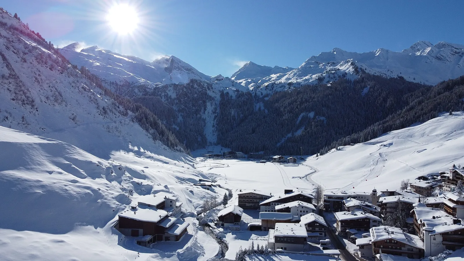 Snötäckta Hintertux längst in i Tuxertal en solig vinterdag, med hus i förgrunden, skog i dalsidorna och glaciärtopparna bakom