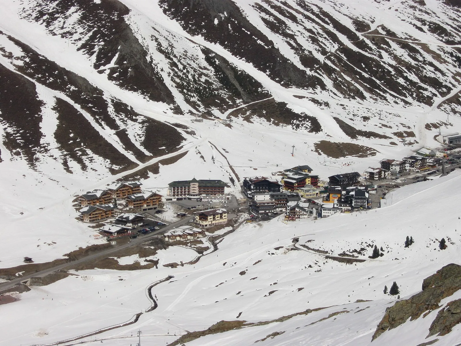 Kühtai sett från ovan en vårdag, en tät samling hotell på 2 000 meters höjd med pister som går ner mot husen från bergen runt omkring