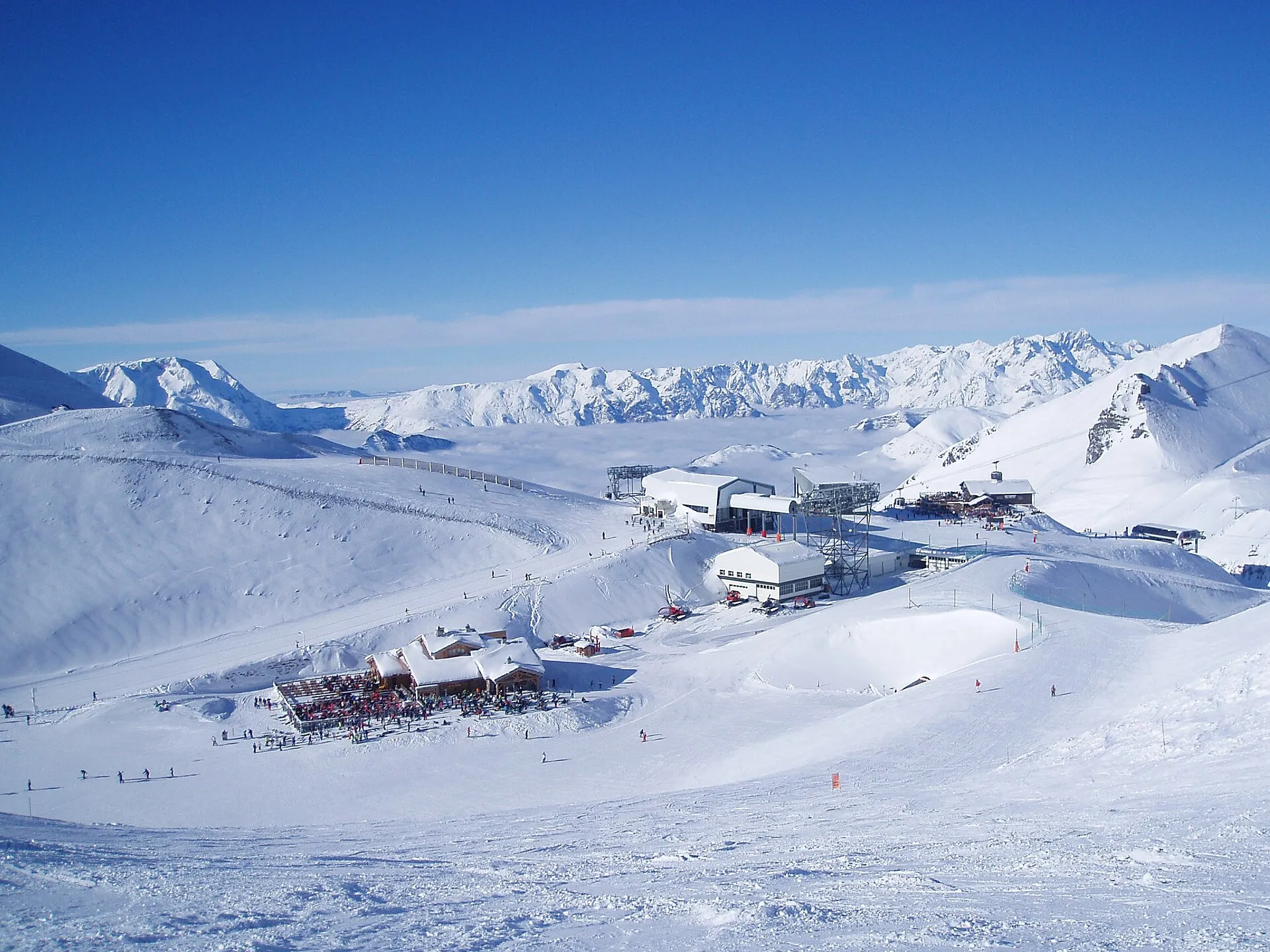Högt uppe i Les Deux Alpes på omkring 3 400 meter, med liftstationer, restauranger och breda pister under en klarblå himmel.