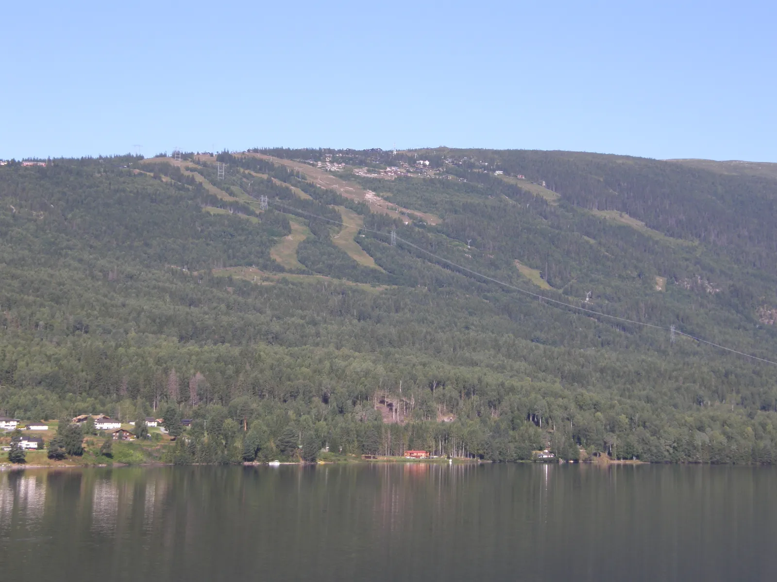 Norefjells skidbackar som långa gröna gator genom skogen från toppen ner mot sjön Krøderen en sommardag