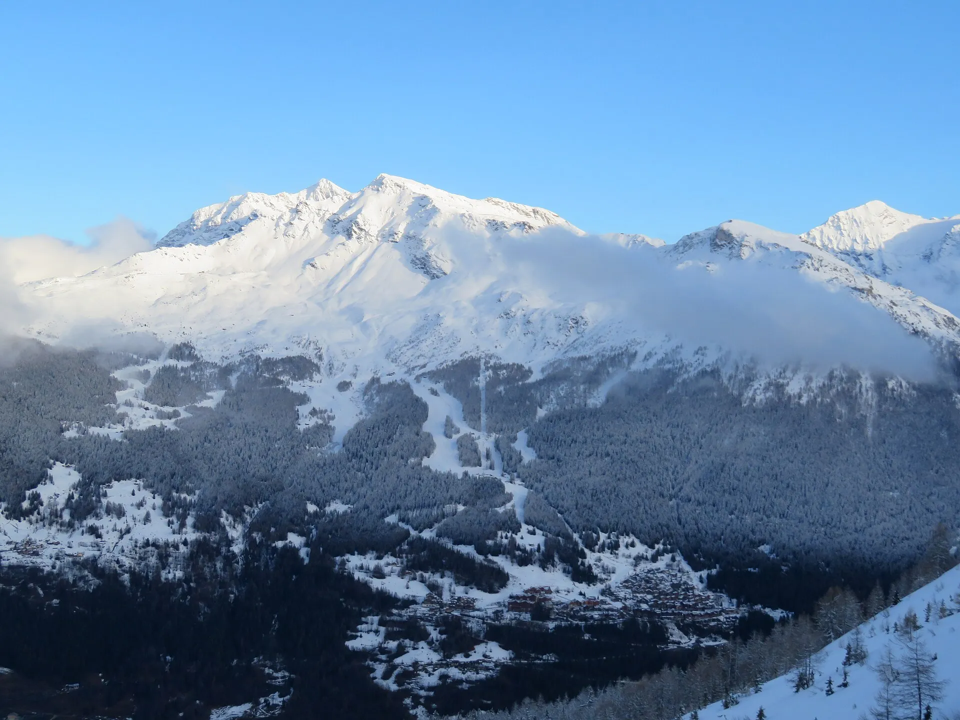 The Sainte-Foy ski area with pistes through the forest below snow-covered peaks, seen from the other side of the valley.