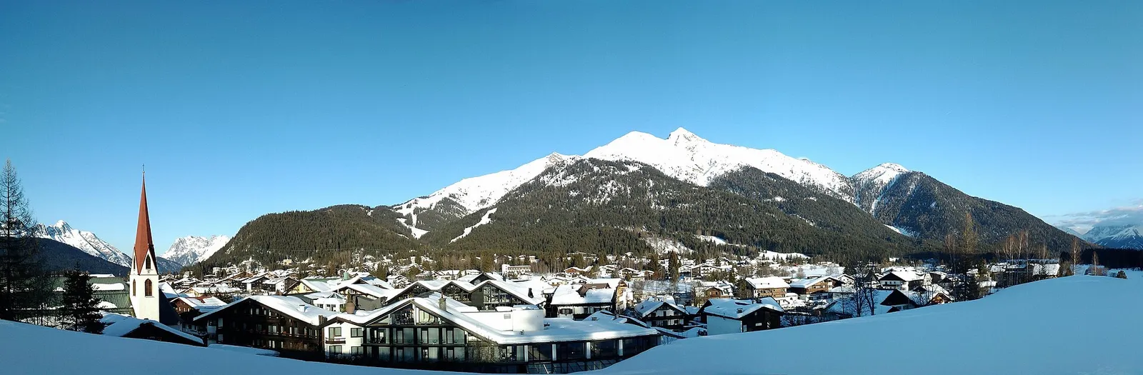 Talvine Seefeld Tiroolis lumiste katuste, vasakul asuva kirikutorni ja metsaste mägedega sinise taeva all