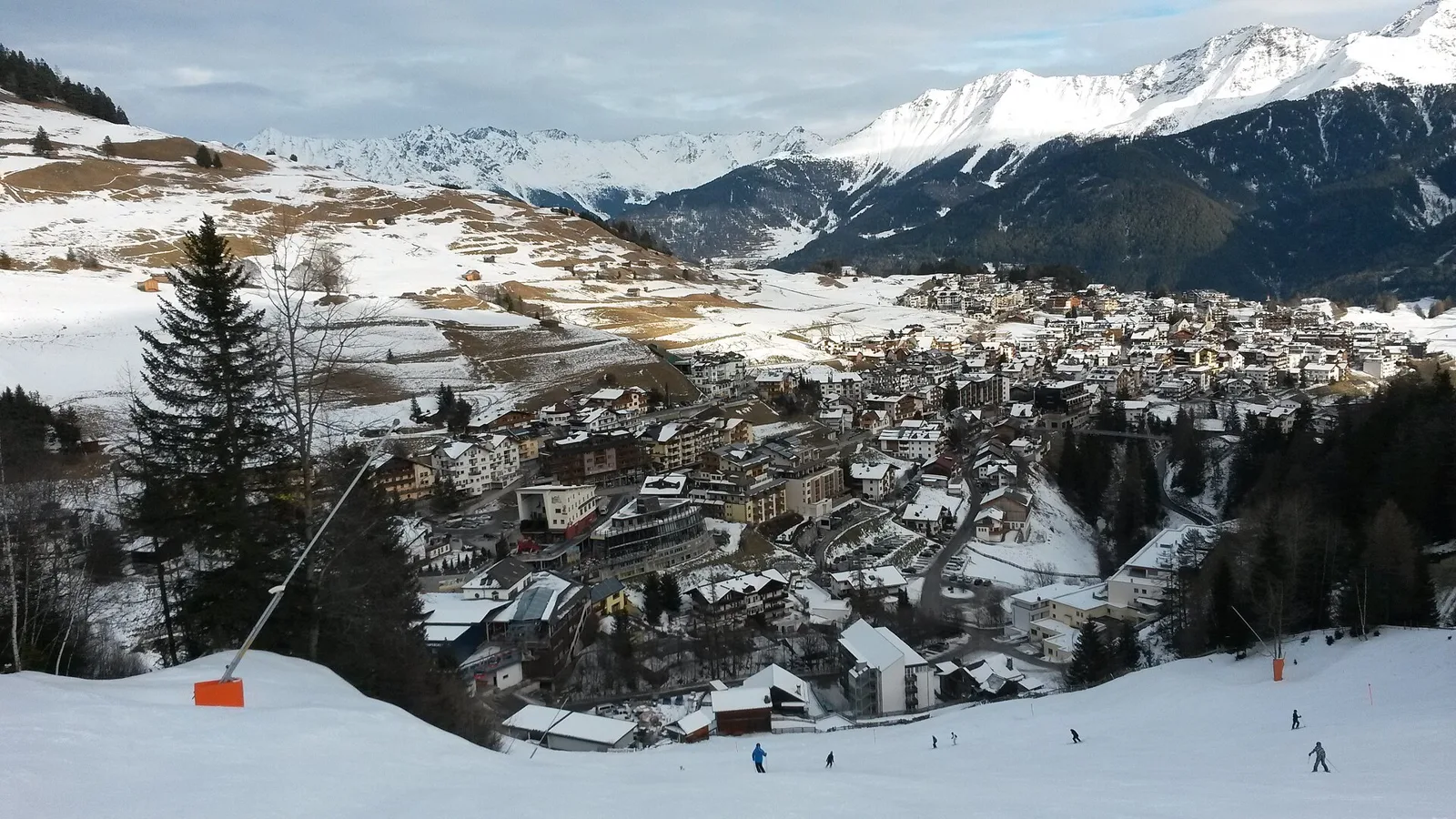 Vinterudsigt over landsbyen Serfaus på plateauet, med pister i forgrunden og snedækkede toppe bagved