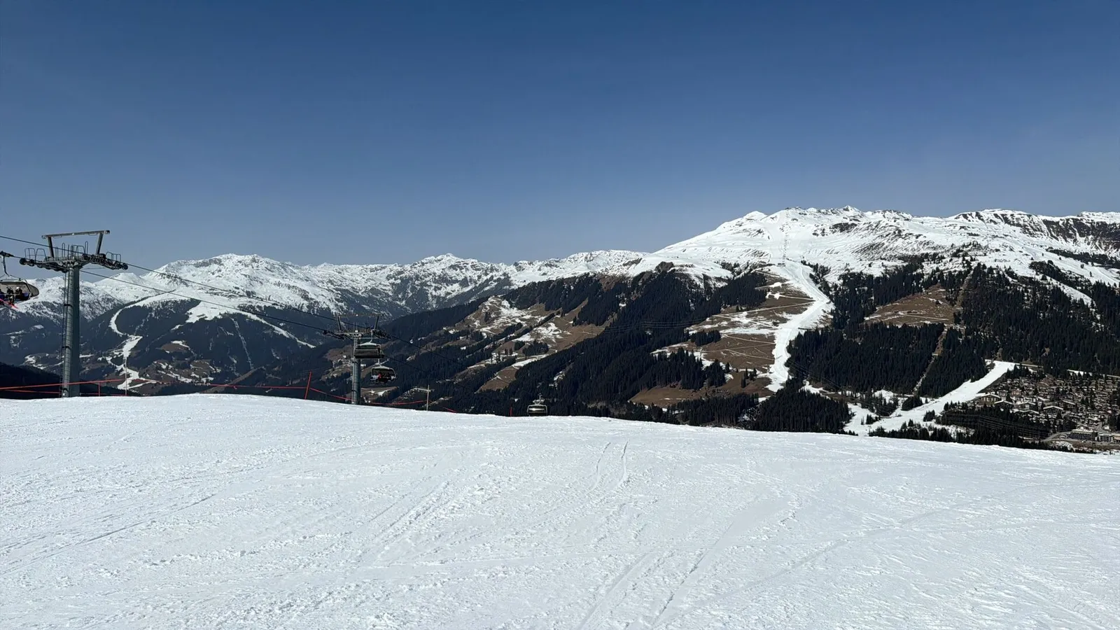 Bred præpareret piste i Zillertal Arena nær Gerlos en solrig senvinterdag med stolelift til venstre og snedækkede bjerge og skovklædte dalsider bagved