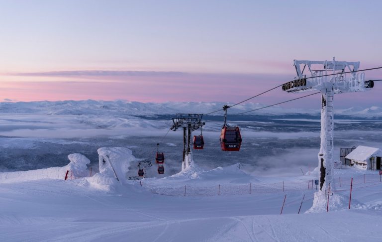 Skidbacke med gondol och snöklädda landskap i skymning.