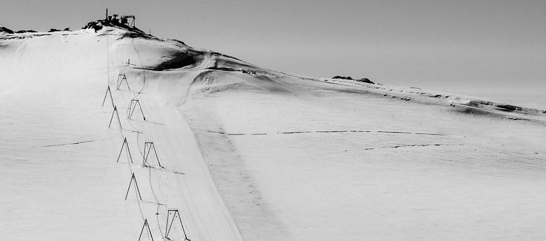 Snötäckta berg med snöspår och staket i förgrunden, svart-vitt.