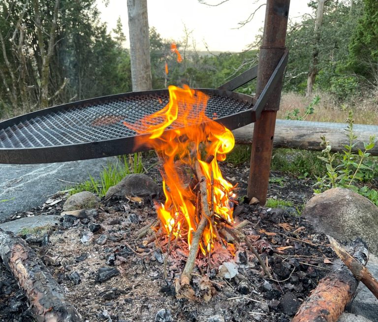 Eldflamma som brinner i en utekamin med aska och stenar runt omkring.