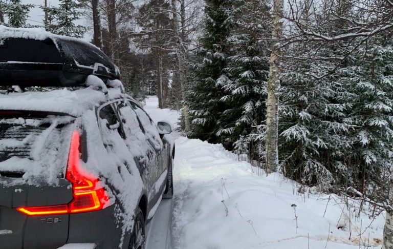En snötäckt väg med en bil parkerad vid sidan av, omgiven av vinterlandskap.