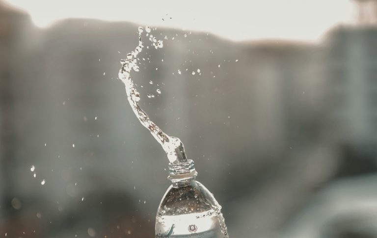 Sprutande vatten från en flasköppning i ett suddigt bakgrundsmiljö.