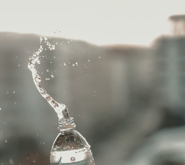 Vattendroppe som stänker från en plastflaska mot en suddig bakgrund.