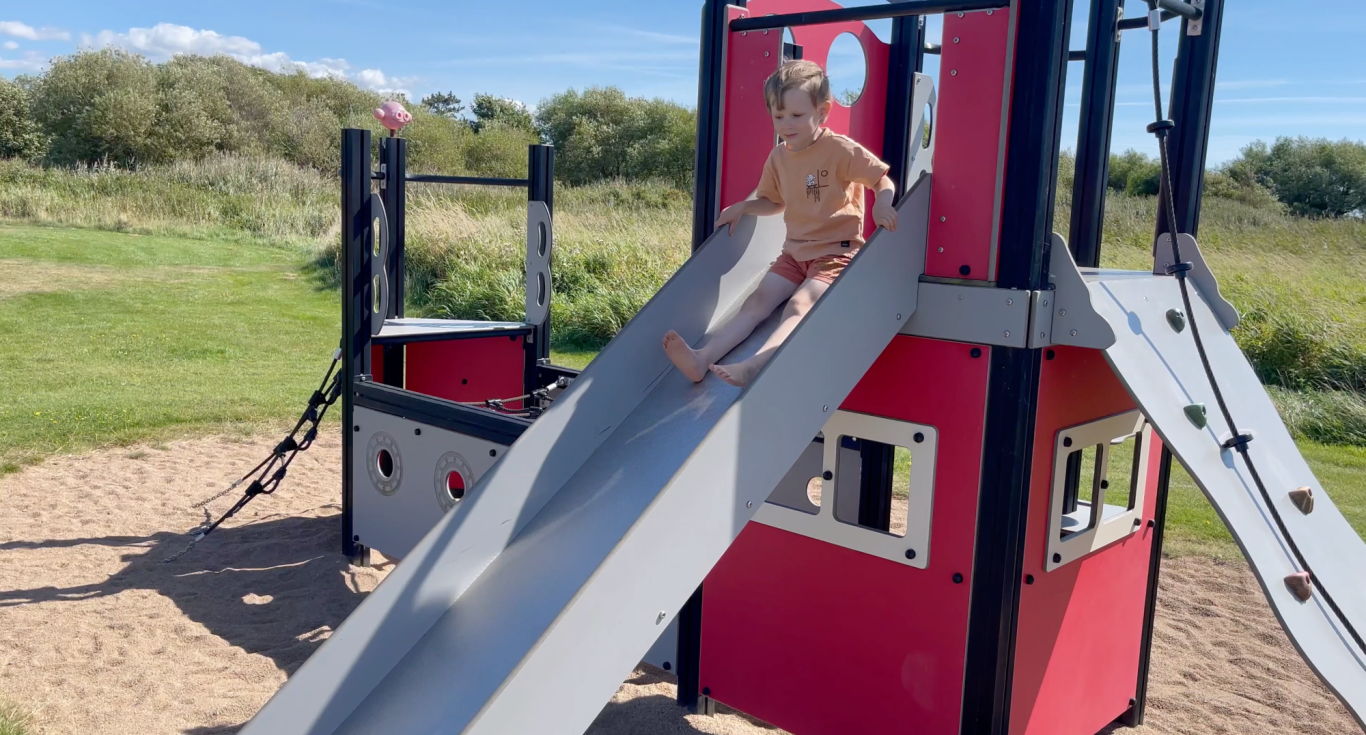 Leker Barn rutschar ner för en glidbanan på en lekplats omgiven av grönska.