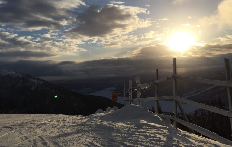 Solnedgång över snötäckta fjäll med en utsiktsplats och moln på himlen.