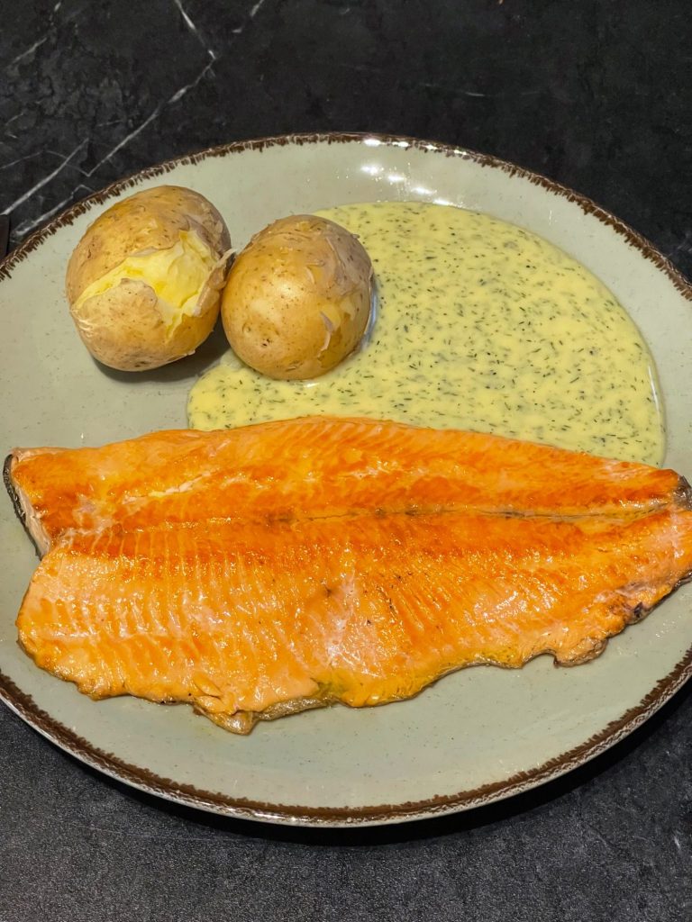 Grillad regnbågsöring med sås, kokt potatis och två hela potatisar på en tallrik.