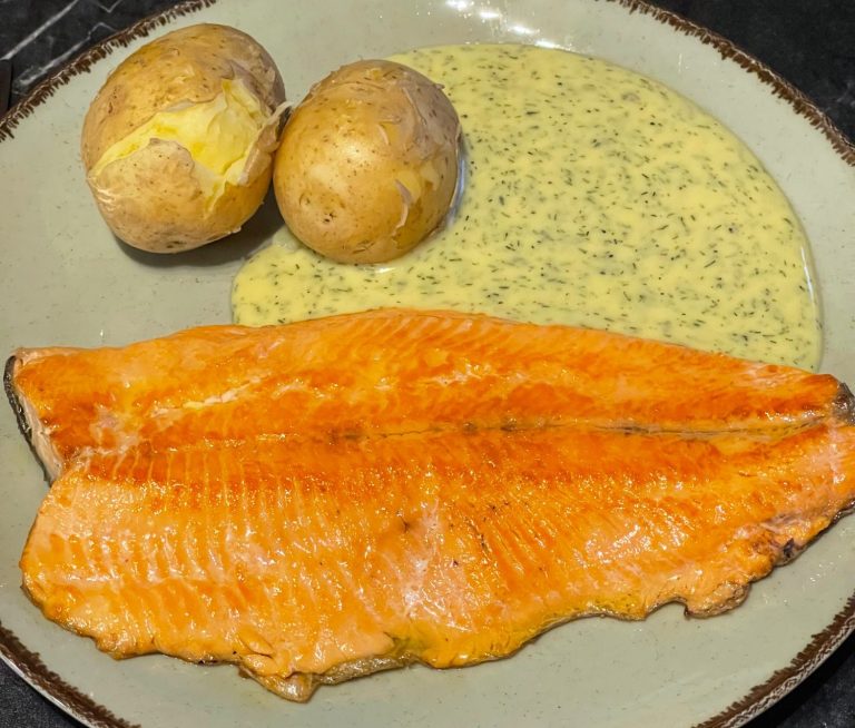 Grillad laxfilé med sås och kokt potatis på en tallrik.