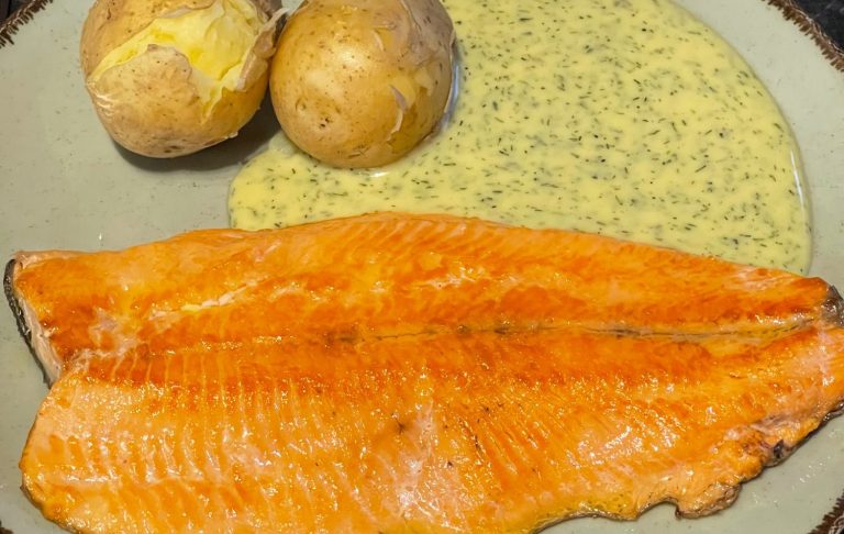 Grillad laxfilé med två potatisar och en grön sås på tallrik.