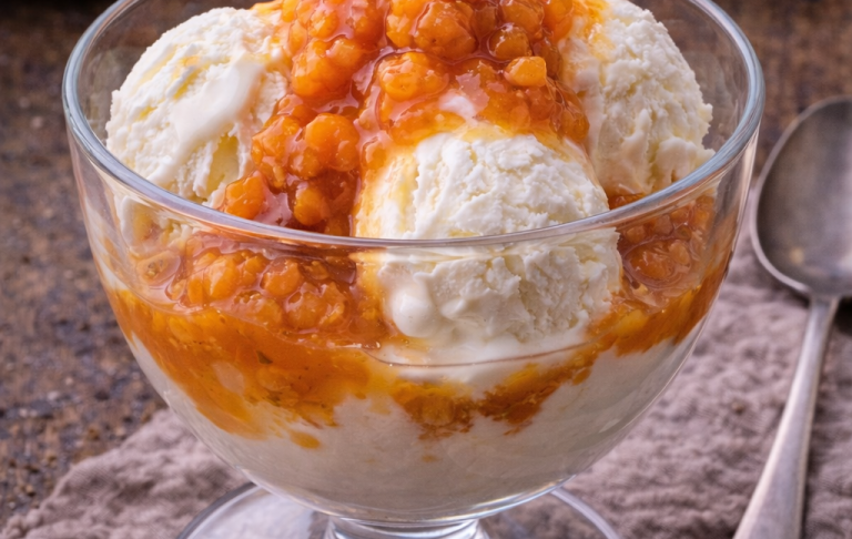 Scoop av vaniljglass toppad med aprikoskompott i en glasdessertskål.