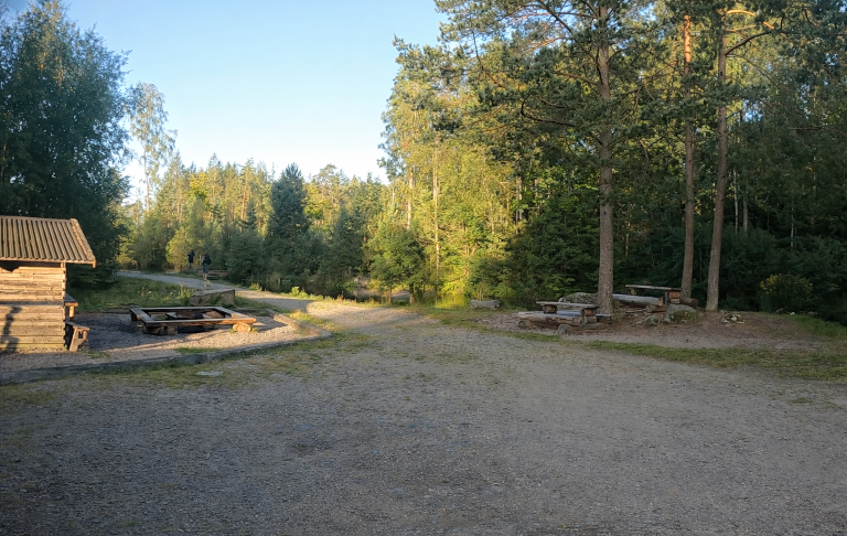 En grusväg omgiven av skog och en liten grillplats med bänkar. Flugströmmen i bakgrunden.
