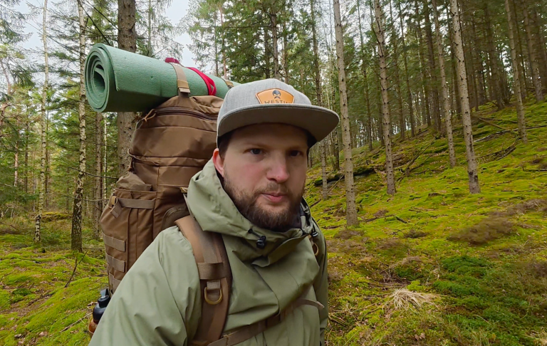 Man med ryggsäck och campingutrustning vandrar i en skog.