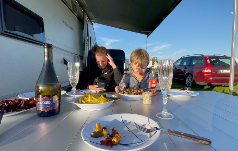 Två personer njuter av mat och dryck vid ett campingbord utomhus.