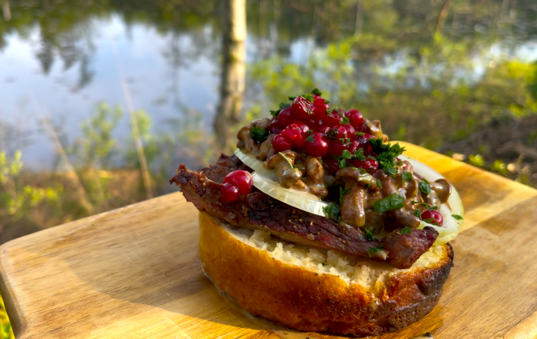 En smörgås med kött, svamp, lökar och granatäpple, placerad vid en sjö.