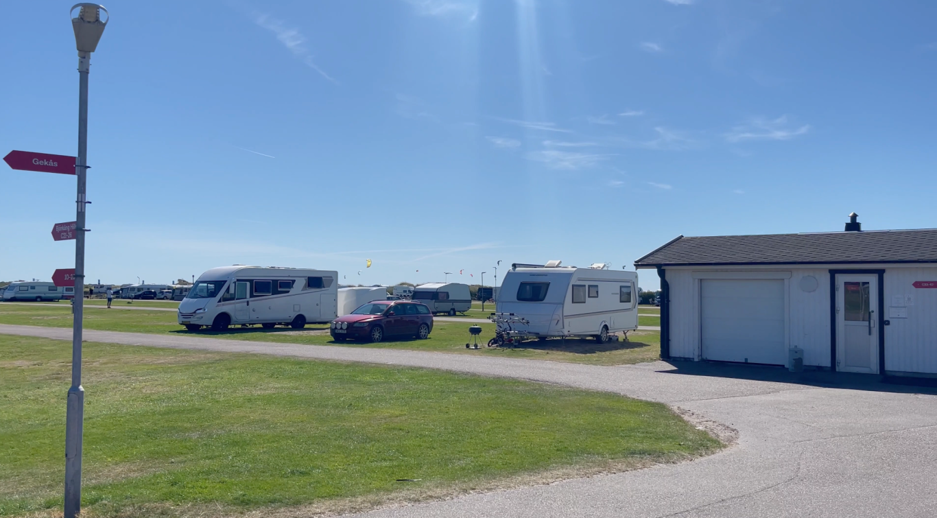 Husvagnen på Campingen Två husbilar parkerade vid en campingplats under klarblå himmel.