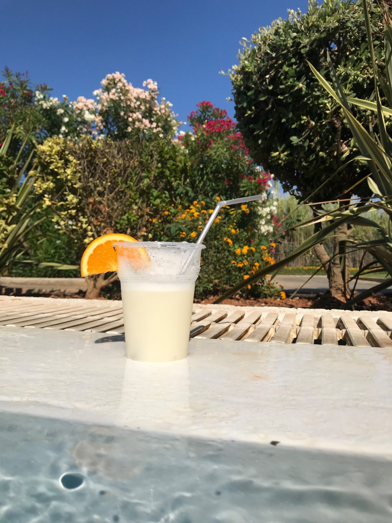 Pina Colada i Poolen En ljus drink med citrus och sugdel, placerad vid en pool med blommor i bakgrunden.