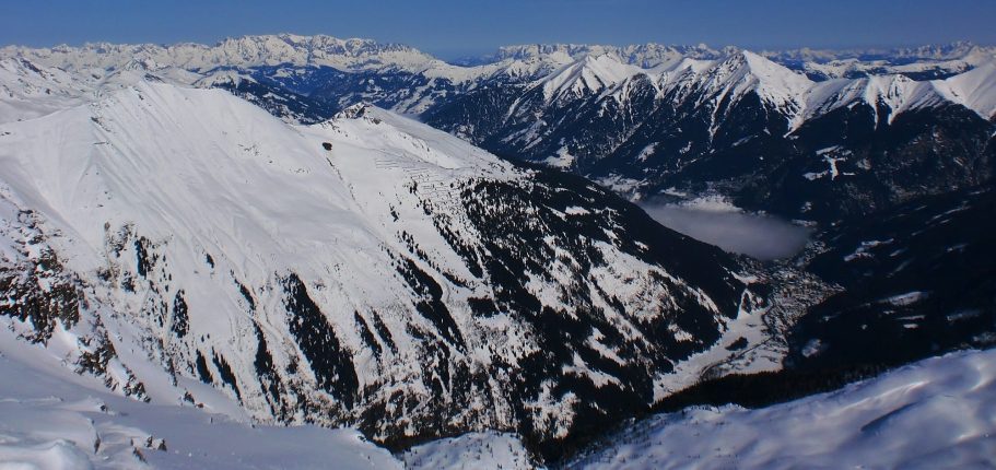 Panoramabild av snöklädda fjäll och solnedgång över dalen.