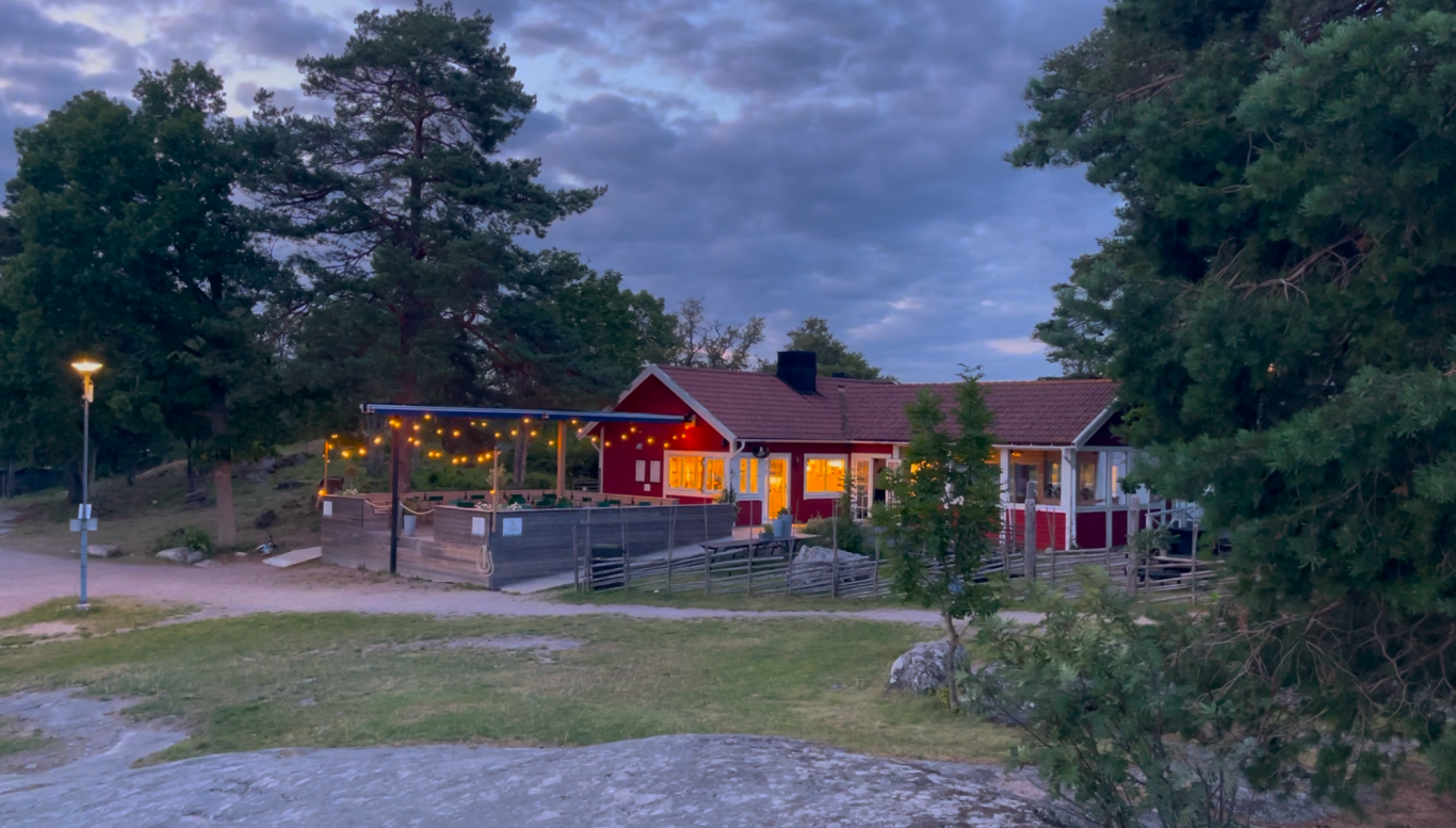 Algots på Udden Stuga med röd fasad, belägen i naturskön miljö vid skymning.