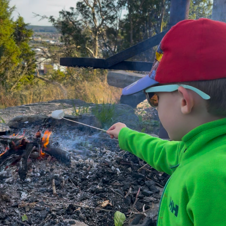 Ett barn lagar marshmallows över öppen eld i naturen Barn i grön tröja rostar marshmallows över en lägereld.