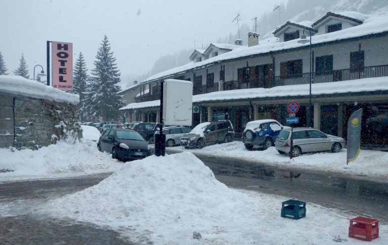 Snötäckt hotellområde med bilar och snödrivor på gatan.