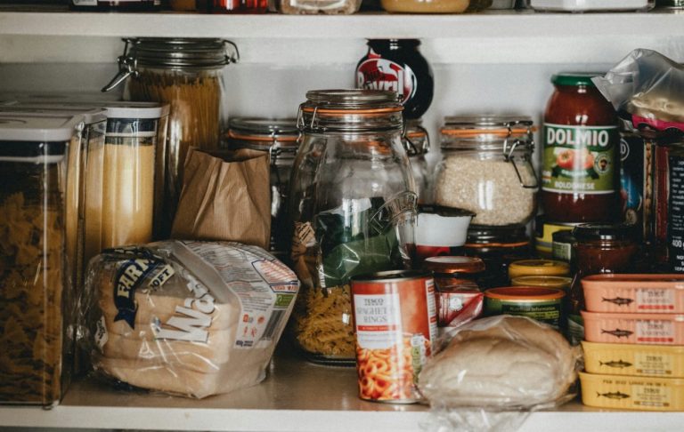 Köksskåp med pasta, konserver, kryddor och olika livsmedelsförpackningar.