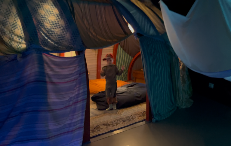 En person står i en färgglad, textilklädd installation med mjuka former.