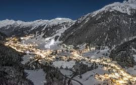Utsikt över en snötäckt dal med belysta hus under natthimlen.