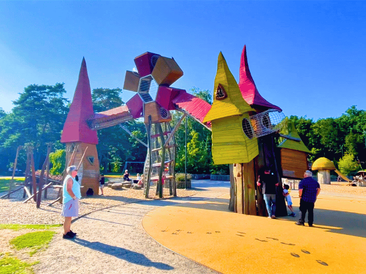 Lekplats med färgglada torn och strukturer, omgiven av grönska och soligt väder.