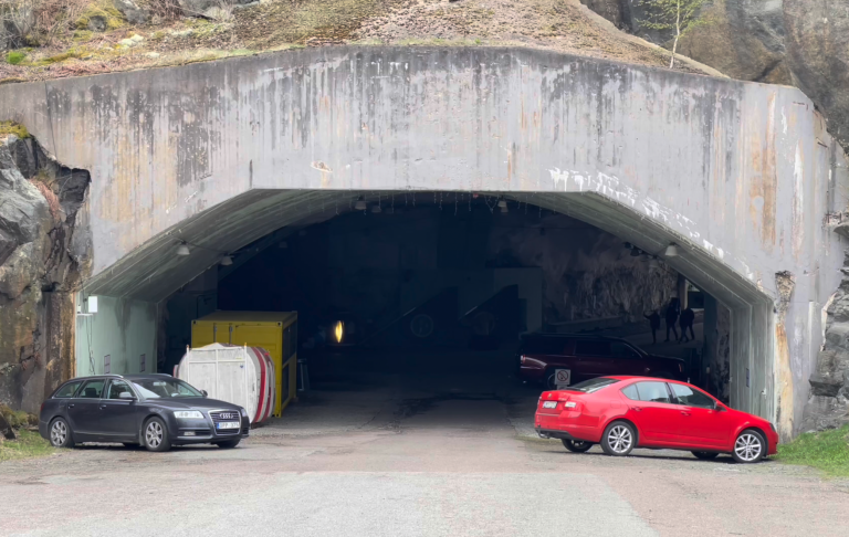 Två bilar parkera vid en stor betongtunnel i en kuperad miljö.