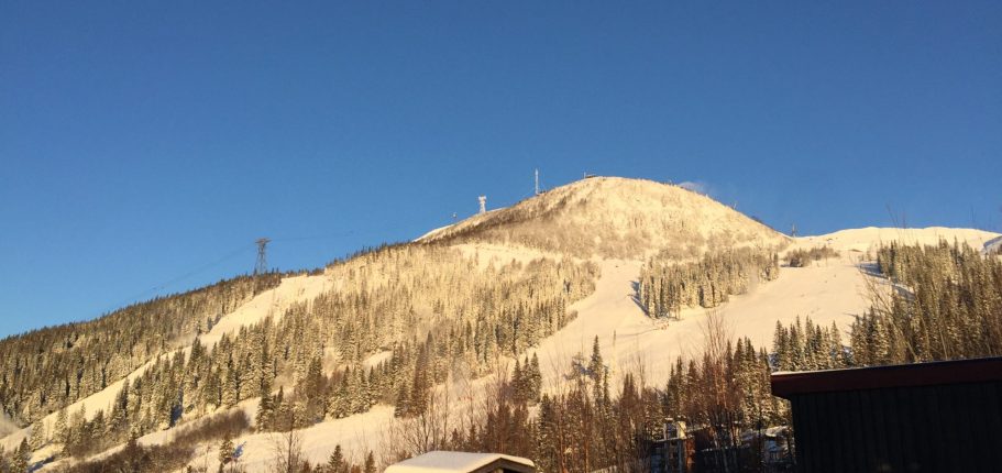 Panoramabild av snöklädda fjäll och solnedgång över dalen.