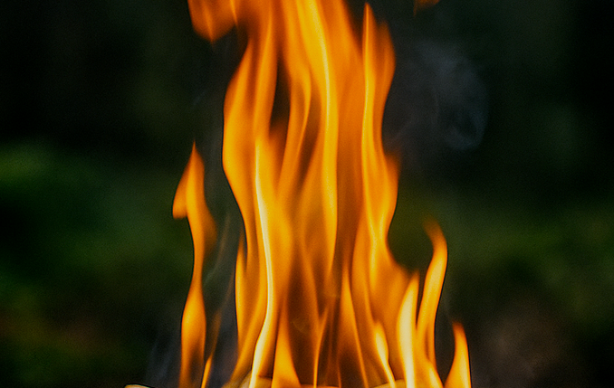 Eld Eldslågor dansar över träbitar i en mörk, suddig bakgrund.