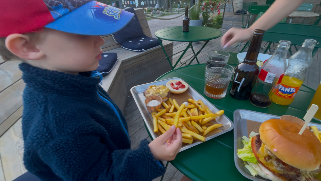 Algots på Udden Barn med keps sitter vid ett bord och äter pomfries och hamburgare.
