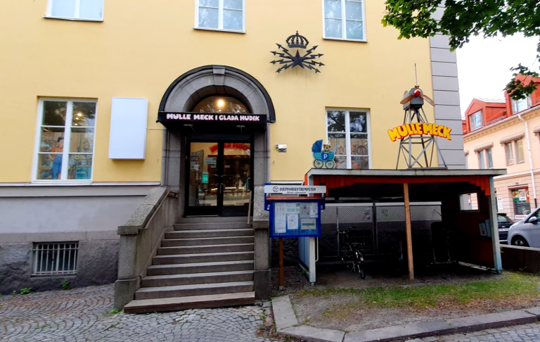 Entré till byggnad med trapport och skyltar utanför, inkl. en liten kiosk.